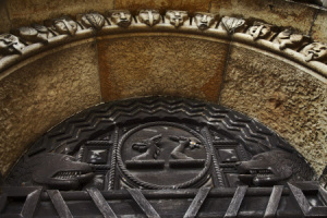 Neo-Norman stonework carving around the door with metalwork crests of the Dawkins and Pennant families, with an antelope's head and an arm with a battle-axe, at Penrhyn Castle, Gwynedd, Wales