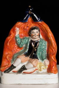 Ceramic, Staffordshire, David Garrick (1717-1779) as Richard III in William Shakespeare's 'Richard III', Staffordshire Pottery. Full-length Staffordshire figure of David Garrick as Richard III, sitting on a couch in a tent, wearing a green coat, black doublet, pink breeches and black boots.