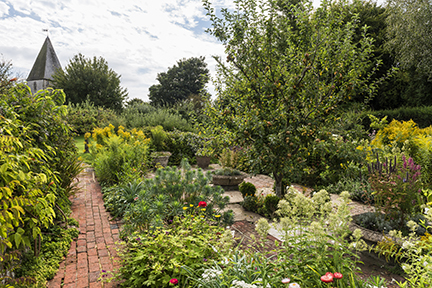 The garden in August at Monk's House, East Sussex. A brick garden path with flowers and trees surrounding.