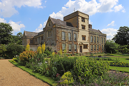 The house and gardens at Canons Ashby, Northamptonshire. Manor home with grass and flower plants in front. Blue sky above