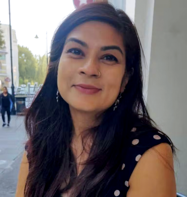 Headshot for Mishka Sinha. Woman with dark, long hear. Wearing a black top with polka dots