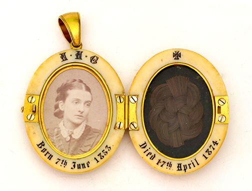 Ivory locket with gold monogram reading, AAG. Gold hinge on one side, gold clasp on opposite site and gold loop on top. Inside the locket on the left is a photograph of a young woman below the initials, AAG. Date around lower edge reads, Born 7th June 1853. The right-hand side contains a lock of plaited hair below the etched date, Died 17th April 1874.